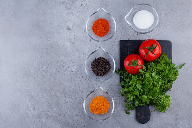 Verse tomaten en peterseliebladeren op zwarte scherpe raad met kruiden.