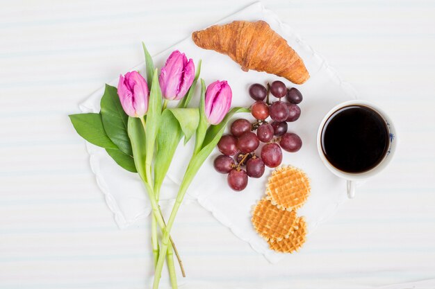 Verse tulpen; croissant; druiven fruit; wafels en theekop op witte achtergrond