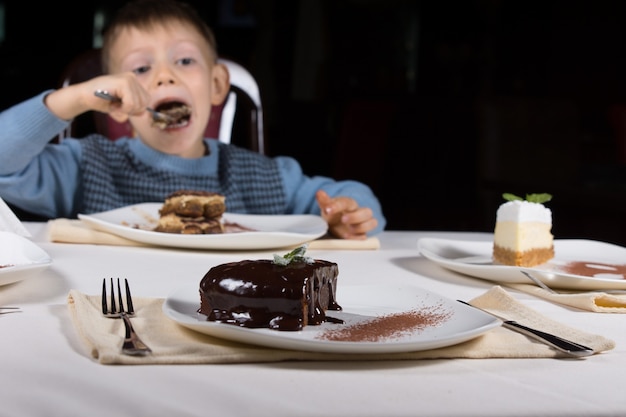 Versgebakken geglazuurde chocoladetaart met een rijke donkere glazuur geserveerd op een bord als dessert met een kleine jongen die cake eet op de achtergrond