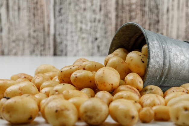 Verspreide aardappelen uit een mini-emmer op witte en grungy houten muur. zijaanzicht.
