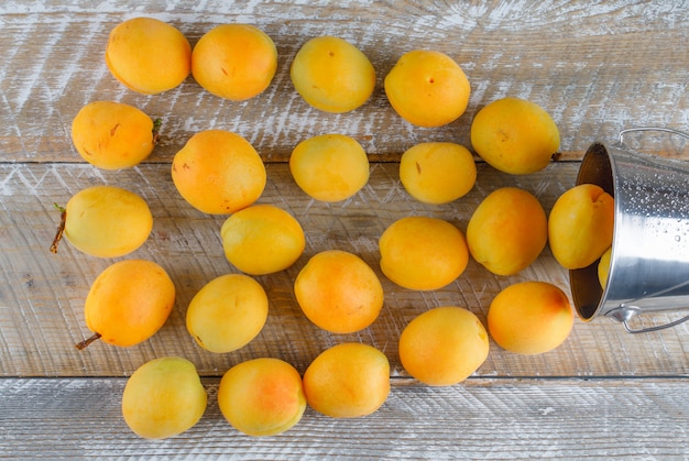 Gratis foto verspreide abrikozen uit mini-emmer op een houten tafel. plat lag.