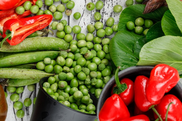 Verspreide erwten uit een emmer met pepers, paksoi, groene peulen close-up op een houten muur