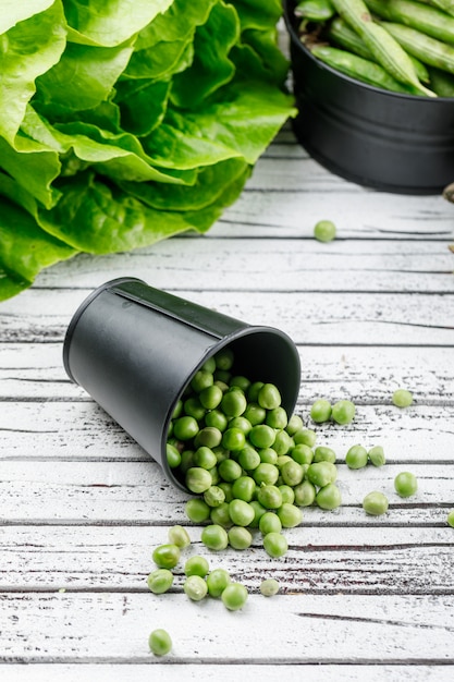 Verspreide erwten uit een emmer met sla, groene peulen hoge hoek uitzicht op een houten muur