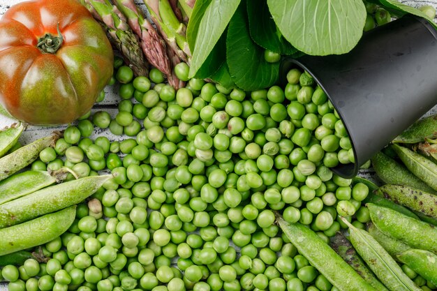 Verspreide erwten uit een mini-emmer met paksoi, groene peulen, tomaat, asperges plat op een houten muur