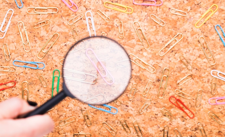 Gratis Foto verspreide paperclips onderzocht door vergrootglas op cork board achtergrond