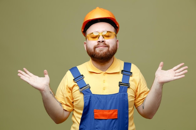 Verspreiden van het verspreiden van handen jonge bouwer man in uniform geïsoleerd op groene achtergrond