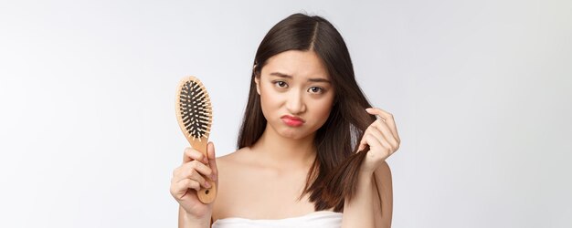 Verstoorde, gestresste jonge Aziatische vrouw die beschadigd droog haar op handen houdt over een witte geïsoleerde achtergrond