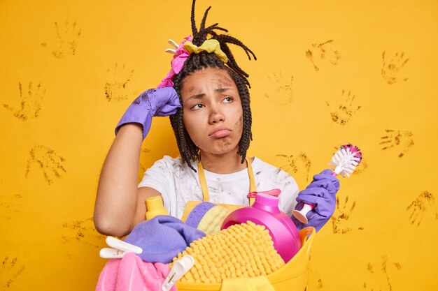 Verstoorde ontevreden vrouw met donkere huid die druk bezig is met de was doet gefrustreerde blik vuil gezicht houdt borstel reinigt toilet poses tegen gele muur
