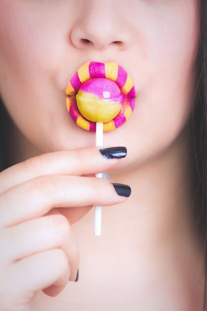 Verticaal close-upschot van een wijfje met een gele en roze lippenstift die een lolly eet