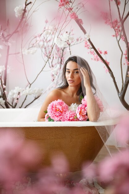 Verticaal portret van een jong heet model zittend in een badkuip rond bloemen Foto van hoge kwaliteit