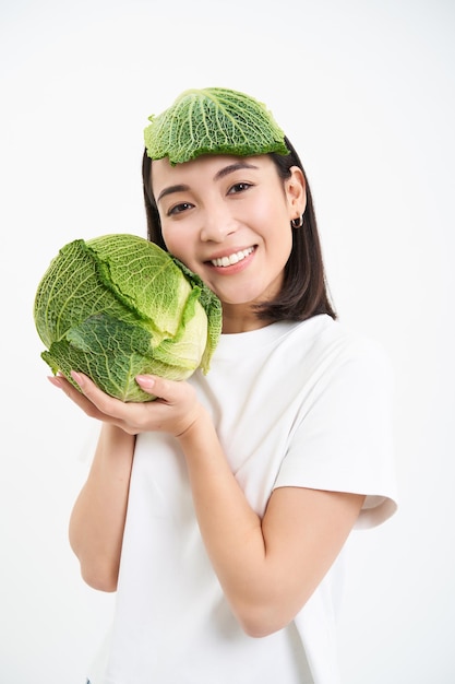 Verticaal portret van glimlachende aziatische vrouw die kool vasthoudt, heeft groen lood op het hoofd, ziet er gelukkig uit, hij