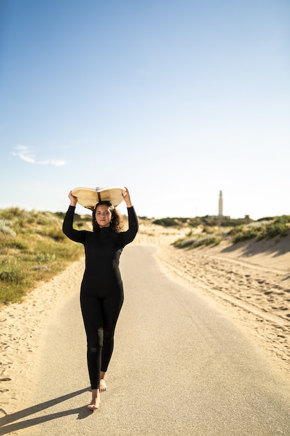 Verticaal schot van een aantrekkelijk wijfje dat een surfplank boven haar hoofd draagt