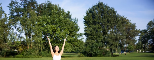 Gratis foto verticaal schot van een aziatische vrouw die haar handen opsteekt naar de hemel, mediteert, yoga beoefent en welzijn doet