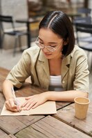 Gratis foto verticaal schot van een jonge aziatische vrouw die huiswerk maakt en notities maakt terwijl ze iets neerschrijft terwijl ze in een