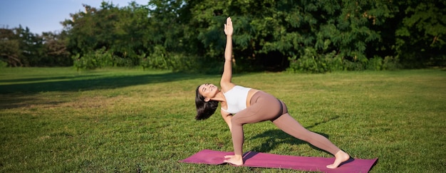 Gratis foto verticaal schot van een jonge koreaanse vrouw die yogatraining doet op een rubberen mat en asana-oefeningen maakt