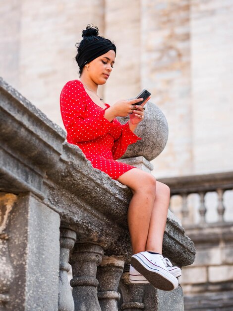 Verticaal schot van een jonge vrouw in rode jurk met mobiele telefoon buitenshuis