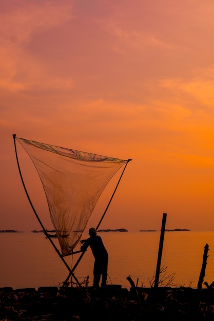 Verticaal schot van een mooie zonsondergang over een overzees met een visser die een net houdt