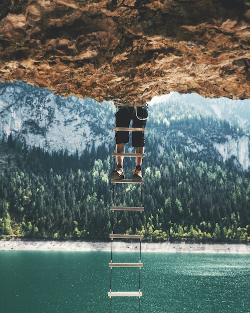 Gratis foto verticaal schot van een persoon die op een ladder beklimt die van een klip hangt