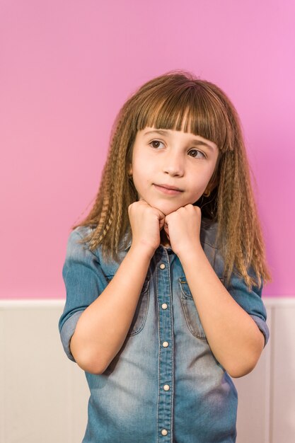 Verticaal schot van een schattig meisje met gekrompen haar en pony poserend voor een roze muur