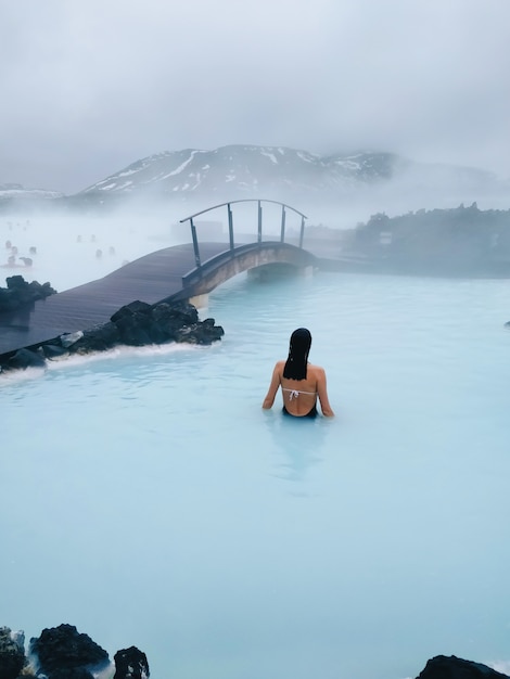 Gratis foto verticaal schot van een vrouw die in een hete pool dichtbij de brug zwemt