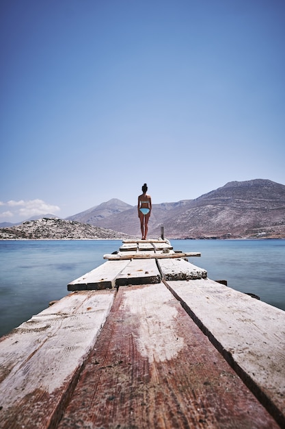 Verticaal schot van een vrouw die zich aan de rand van een houten dok in Amorgos-eiland, Griekenland bevindt