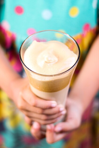 Verticaal schot van een vrouw met kleurrijke kleding die een karamel-smoothie in haar handen houdt