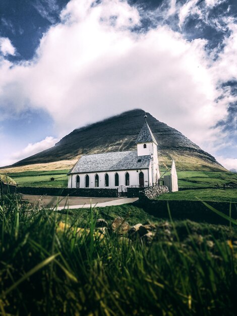 Verticaal schot van een wit huis met grijs dak op groene grasgrond met een berg