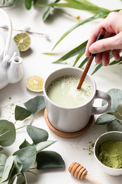 Verticaal schot van Groene thee latte met melk in een witte kop met groene bladeren en houten lepel