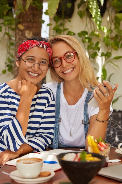 Verticaal schot van multi-etnische vrouwen omhelzen, zitten samen in coffeeshop