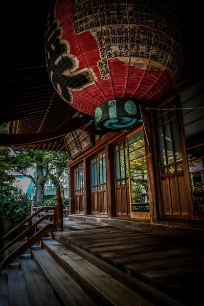 Verticaal schot van rode lantaarn over de treden dichtbij het houten huis in Japanse stijl