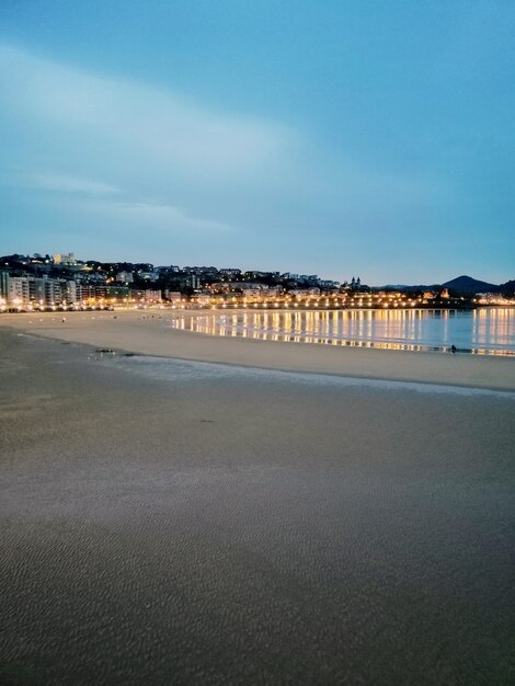 Verticaal schot van stadslichten die in de oceaan in San Sebastian, Spanje nadenken