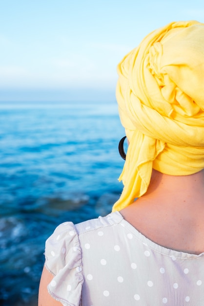 Verticaal schot van vrouw met een gele sjaal, genietend van het uitzicht op zee