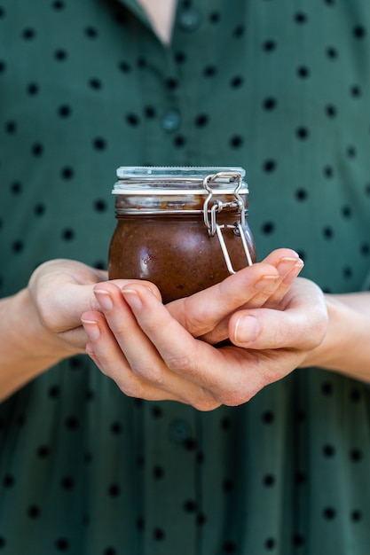 Verticaal schot van vrouwelijke handen met een zelfgemaakte veganistische rauwe pruimenjam in een glazen pot