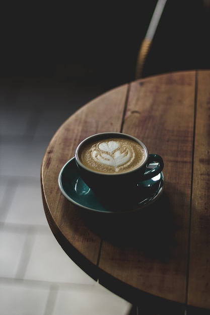 Verticaal selectief close-upschot van koffie met lattekunst in een blauwe ceramische kop op een houten lijst