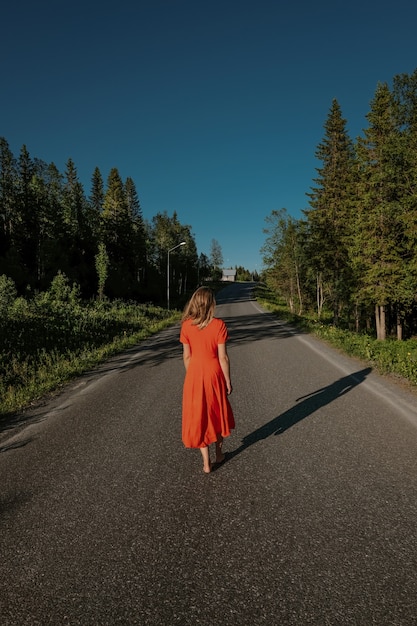Verticale achteraanzicht van een vrouw in een jurk die op een pad loopt, omringd door bomen