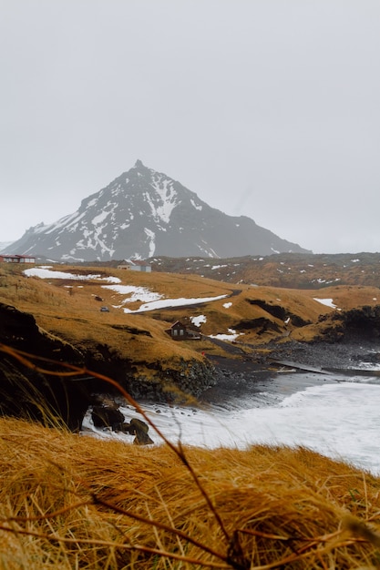 Verticale afbeelding van een rivier omgeven door heuvels bedekt met sneeuw en groen in IJsland