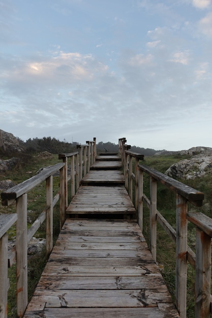 Verticale afbeelding van houten trappen in een veld omgeven door groen en heuvels onder een bewolkte hemel