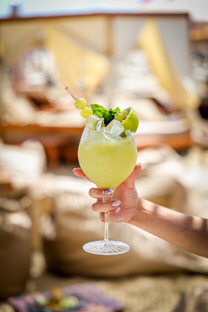 Verticale close-up van een fruitige cocktail met druiven, limoenmunt en ijsblokjes op een strand