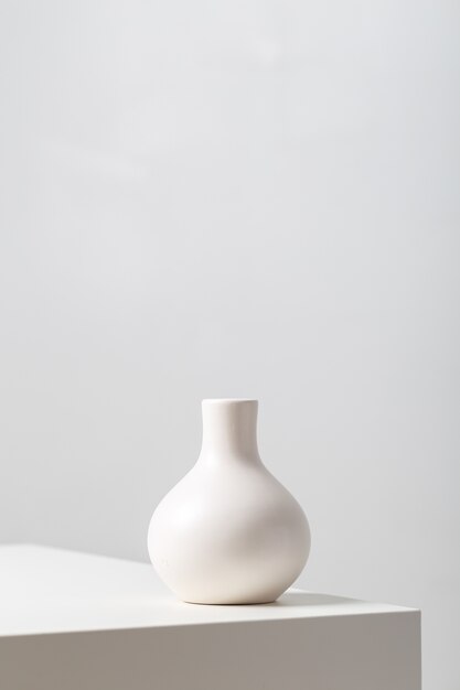 Verticale close-up van een witte klei vaas op de tafel onder de lichten tegen een witte achtergrond