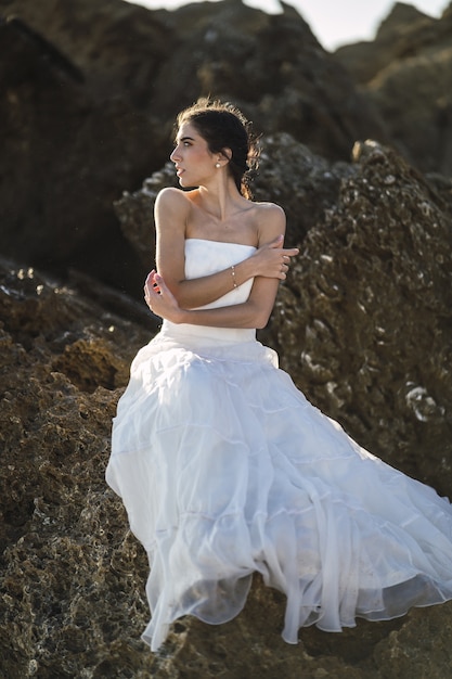 Verticale foto van een brunette vrouw in een witte jurk die zich voordeed op de rotsen