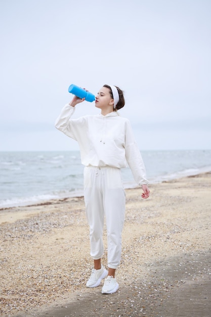 Verticale foto van een jong meisje dat op het strand staat en water drinkt Foto van hoge kwaliteit