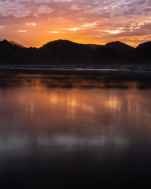 Gratis foto verticale opname van de zee met bergen in de verte bij zonsondergang