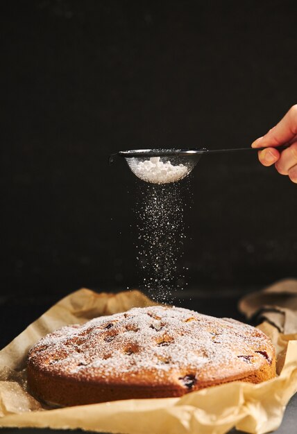 Verticale opname van een Cherry Cake met suikerpoeder en ingrediënten aan de zijkant op een zwarte achtergrond