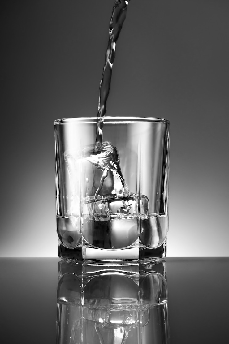 Gratis Foto verticale opname van een drankje dat in een glas met ijs wordt gegoten