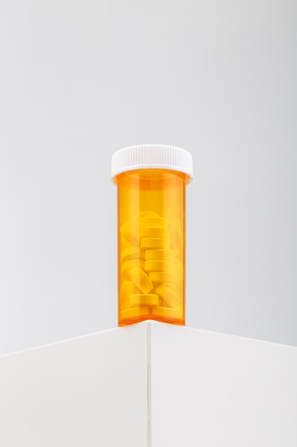 Gratis foto verticale opname van een gele container gevuld met pillen op een witte tafel