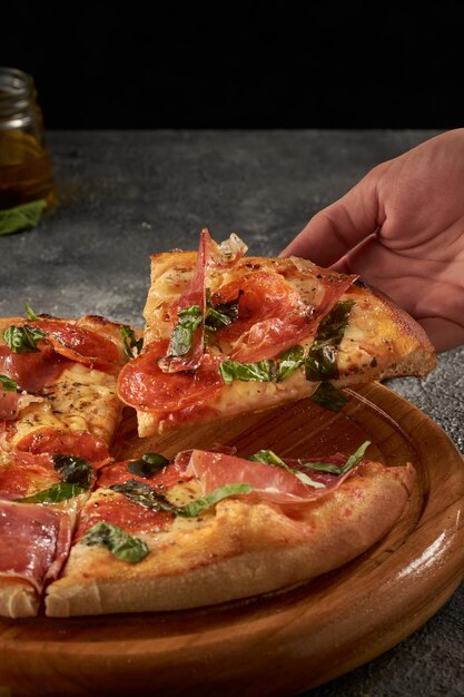 Verticale opname van een hand die een stuk heerlijke prosciutto-pizza grijpt