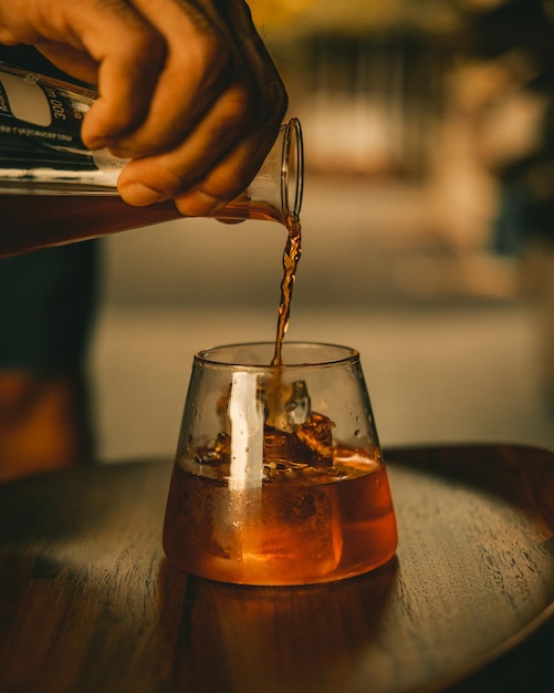 Verticale opname van een hand die sap in een glas met ijsblokjes giet