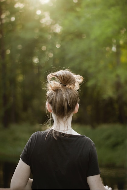 Verticale opname van een jonge blonde vrouw in een zwart shirt die naar het prachtige groen kijkt