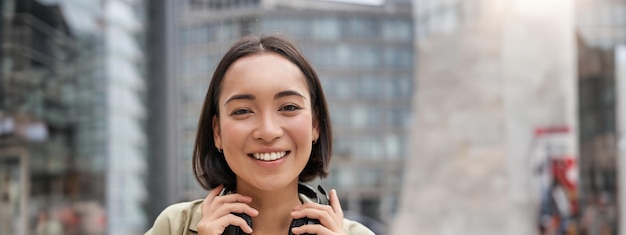 Gratis foto verticale opname van een mooie aziatische vrouw die met een koptelefoon om de nek poseert en glimlacht en lacht