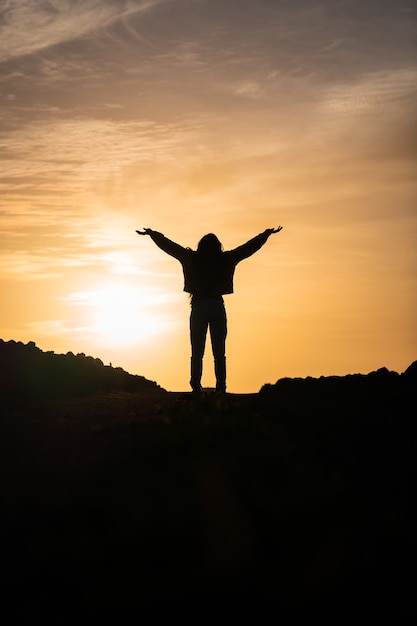 Gratis foto verticale opname van een persoon met de handen omhoog tegen de achtergrond van de zonsondergang